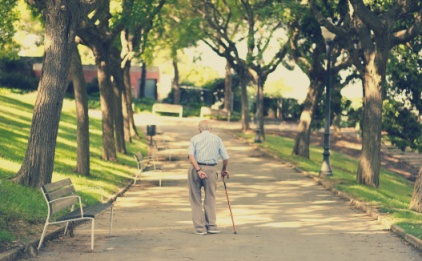 Imagen de un anciano con un bastón y de espaldas paseando por un parque